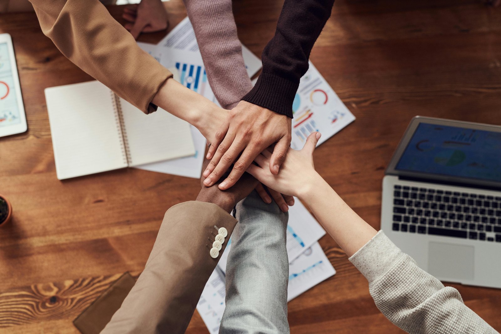 Home Diverse professionals unite for teamwork around a wooden table with laptops and documents.